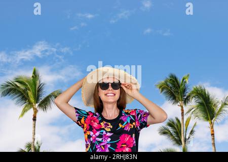 Frau mit Sonnenhut und Sonnenbrille vor Palmen und blauem Himmel, Reisehintergrund, Sommerurlaub Stockfoto