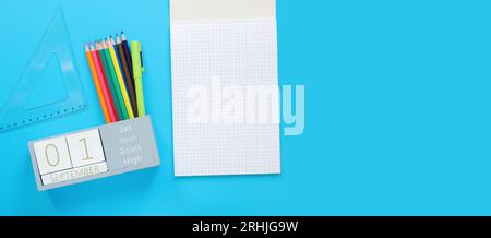 September. Bild eines Holzkalenders für den 1. September auf einem blauen Tisch, Draufsicht. Zurück zur Schule. Kalender, Stifte und ein offenes Notizbuch. Schreibwaren Stockfoto