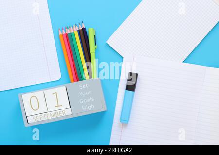 September. Bild eines Holzkalenders für den 1. September auf einem blauen Tisch, Draufsicht. Zurück zur Schule. Kalender, Stifte und ein offenes Notizbuch. Schreibwaren Stockfoto