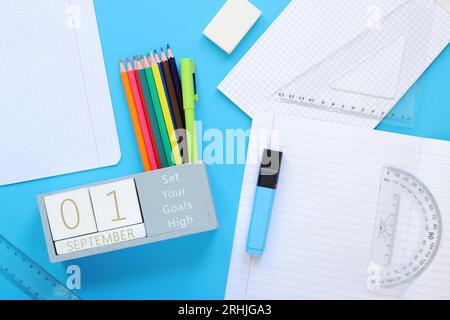 September. Bild eines Holzkalenders für den 1. September auf einem blauen Tisch, Draufsicht. Zurück zur Schule. Kalender, Stifte und ein offenes Notizbuch. Schreibwaren Stockfoto