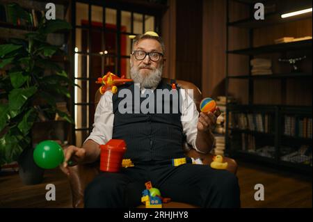 Porträt eines reichen Geschäftsmanns, der mit Spielzeug in einem Ledersessel sitzt Stockfoto