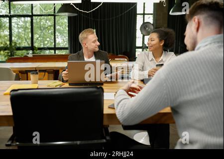Geschäftsleute, die Gadgets verwenden, sprechen und lächeln während einer Besprechung im Büro Stockfoto