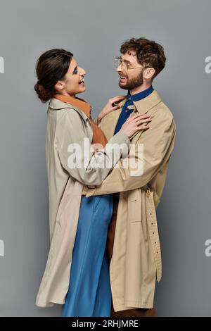 Herbstsaison, glücklicher Mann und Frau, die sich auf grauem Hintergrund umarmen, Paar in Trenchcoat, Stil, Romantik Stockfoto