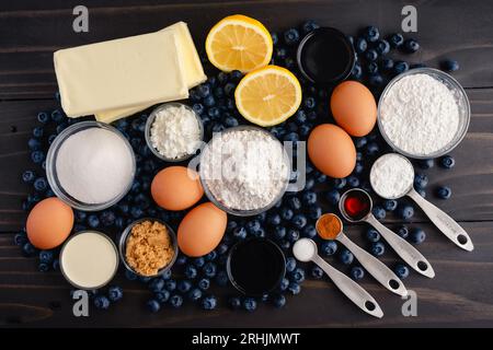 Blaubeere Kobbler Kuchen Zutaten auf einem dunklen Holztisch: Frische Heidelbeeren, Zitronen und andere rohe Zutaten auf einem rustikalen Holzgrund Stockfoto