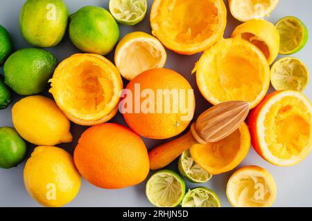 Ganze und entsaftete Zitrusfrüchte mit einem Zitrussammelgerät aus Holz: Ein manueller Entsafter, umgeben von ganzen und halben Orangen, Zitronen und Limetten Stockfoto