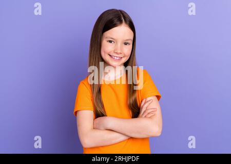 Foto von Tochter süße Vorschulmädchen tragen orange T-Shirt überkreuzte Hände selbstbewusste Spezialisten spielen Spiele isoliert auf lila Farbe Hintergrund Stockfoto