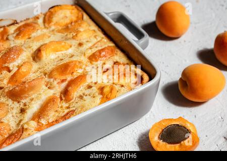 Clafoutis mit Aprikose - Sommerkuchen in einer Auflaufform und frische Aprikosen auf dem hellen Tisch Stockfoto