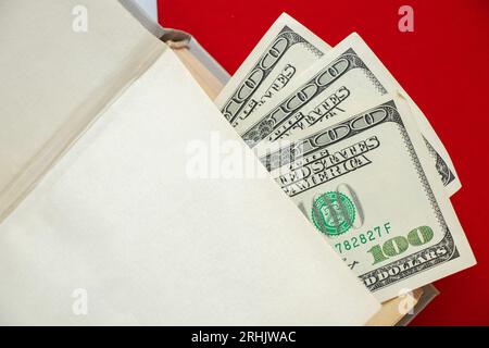 Hundert Dollar-Rechnungen liegen in einem Buch vor dem Hintergrund eines roten Buches, Wirtschaft und Bildung Stockfoto