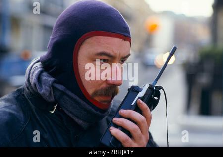 Walkie Talkie 1990s UK Motorcycle Dispatch Rider erhält eine Nachricht über seinen altmodischen Retro-Funkempfänger – Walkie Talkie, der die Motorradbatterie abgeschaltet hat. Tragen Sie eine Kapuze aus Balaclava für Wärme und Schutz. London. Eine Nachricht von einem altmodischen Radio aus den 1990er Jahren HOMER SYKES Stockfoto