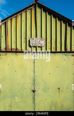 Abstraktes Bild eines alten Metallgebäudes, grün mit Rost und Schattierungen bemalt, Sea Cadet-Schild auf der Außenseite. Farbenfrohe abstrakte Farben. Texturen. Rostig. Stockfoto