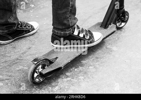 Ein Junge auf einem Roller in einem Skatepark spielt Sprünge und Tricks. Extrem städtischer Outdoor-Sport, gesundes Lifestyle-Konzept. Sportliche Freizeitangebote. Schwarz auf Weiß Stockfoto