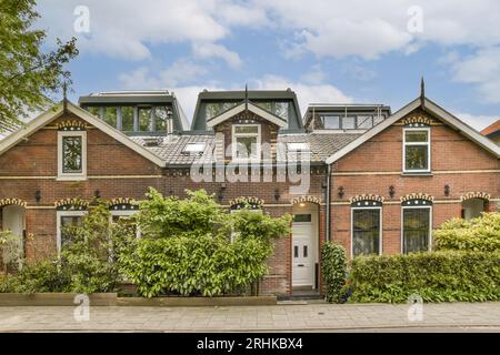 Ein Haus in den niederlanden mit einer orangen Ziegelfassade und grünen Pflanzen, die auf dem Vorhof wachsen, umgeben von Bäumen Stockfoto