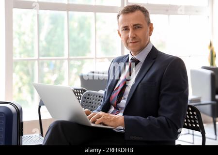 Reifer Geschäftsmann mit Laptop in der Halle des Flughafens Stockfoto
