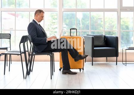 Reifer Geschäftsmann mit Laptop in der Halle des Flughafens Stockfoto