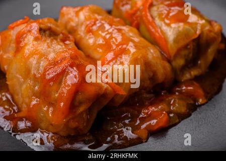 Köstliches Dolma in Tomatensauce mit Karotten, Zwiebeln, Salz, Gewürzen und Kräutern auf dunklem Betonhintergrund Stockfoto