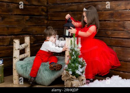 Ein kleines Mädchen und ein Junge schauen sich die Weihnachtskerze an. Holzhintergrund. Vorbereitung auf Neujahr und Weihnachten. Ein fröhliches kleines Mädchen schaut auf die Stockfoto