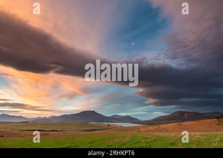 Wunderschöner dramatischer rosa bewölkter Sonnenuntergang über Villiersdorp Tal und Theewaterskloof Damm Stausee mit Bergketten in Overberg, Western Cape Stockfoto