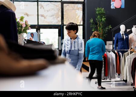 Manager bereitet den Laden für die Eröffnung vor und arrangiert stilvolle Kleidung für Kunden in einer modernen Boutique. Mitarbeiter im Einkaufszentrum, der modische Waren überprüft und mit trendigen Artikeln arbeitet Stockfoto
