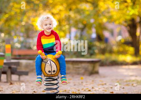 Kinder auf dem Spielplatz Kinder spielen im Herbstpark. Kind auf Rutsche und Schaukel am sonnigen Herbsttag. Vorschule oder Kindergarten. Kindertagesstätte für junge Kinder. Stockfoto