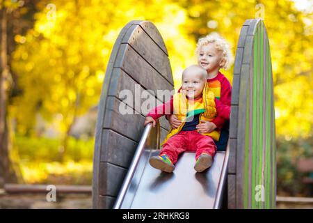 Kinder auf dem Spielplatz Kinder spielen im Herbstpark. Kind auf Rutsche und Schaukel am sonnigen Herbsttag. Vorschule oder Kindergarten. Kindertagesstätte für junge Kinder. Stockfoto