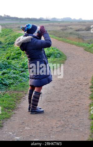 Ältere Rentnerin, die mit einem Fernglas über die Sümpfe von blakeney in norfolk england blickt Stockfoto