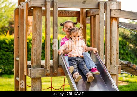 Die Schwestern gleiten zusammen auf einem Spielplatz - Kinder haben Spaß miteinander Stockfoto