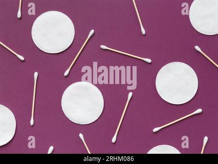 Wattepads, Schwämme und Wattestäbchen befinden sich auf einem fliederfarbenen Hintergrund, Draufsicht. Hygiene, Make-up, Medizin. Stockfoto