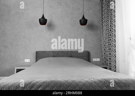 Modernes Design des Schlafzimmers in Grautönen, Minimalismus im Inneren. Ein großes Bett im Schlafzimmer, Nachttische mit schwarzem Glas, schwarze Kronleuchter Stockfoto