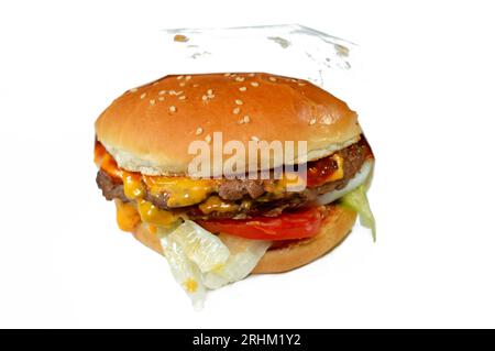 Ein saftiges, dickes, doppeltes Rinderpatty mit Käse, der mit Sauce bedeckt ist, knackigem Salat, frischen Tomaten, Zwiebeln und Gurken in einem großen Sesambrötchen, einem Rindfleisch Stockfoto