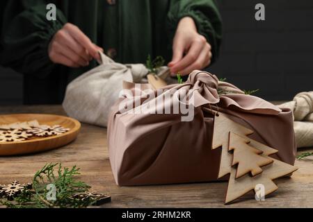 Eingewickelt in Stoffgeschenk mit Thuja-Zweigen auf Holztisch. Frau mit Furoshiki-Technik, selektiver Fokus Stockfoto