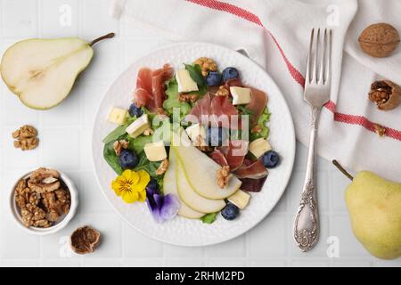 Leckerer Salat mit Brie-Käse, Prosciutto, Walnüssen und Birne serviert auf weißem Fliesentisch, flach gelegt Stockfoto