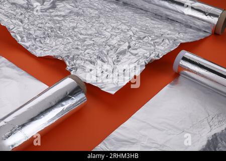 Verschiedene Rollen Aluminiumfolie auf orangem Hintergrund, Nahaufnahme Stockfoto