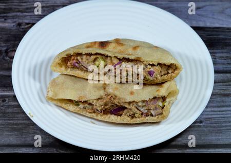 Ein flaches Brot mit pürierten Fava-Bohnen, gemischt mit Öl, Sesam-Tahini, Kreuzkümmel, Gewürzen, Scheiben Chilischeffer und Zwiebeln, selektiver Fokus auf traditionellen Pop Stockfoto