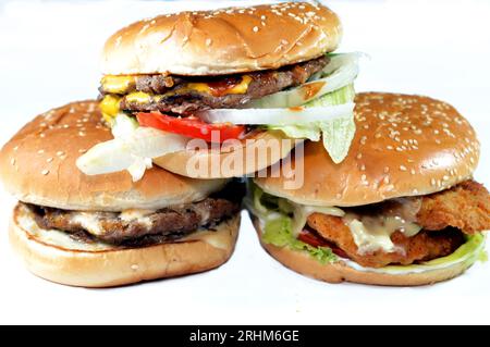 Haufen Sesambrötchen mit frittierten panierten Hähnchenfilet-Pattys, knackigem Salat, Schmelzkäse, Zwiebeln und Sauce, saftigem, dickem, doppeltem Rinderpatty mit Chees Stockfoto