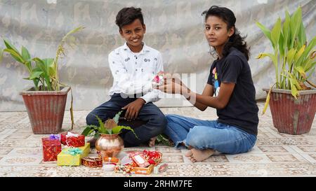 Die indische Schwester bindet Rakhi an das Handgelenk ihres kleinen Bruders und tauscht Geschenke und Süßigkeiten auf dem Raksha Bandhan oder Bhai Dooj Festival aus Stockfoto