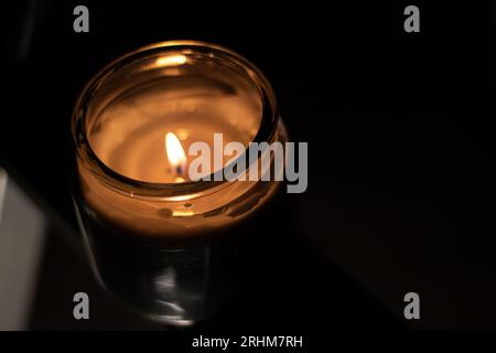 Nahaufnahme Der Kerzenflamme In Transparentem Glas - Hochwinkelaufnahme. Nahaufnahme der Flamme, die auf der Kerze brennt, isoliert auf schwarzem Hintergrund. Kerzenflamme herein Stockfoto