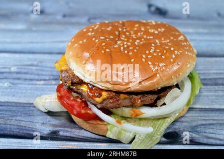 Ein saftiges, dickes, doppeltes Rinderpatty mit Käse, der mit Sauce bedeckt ist, knackigem Salat, frischen Tomaten, Zwiebeln und Gurken in einem großen Sesambrötchen, einem Rindfleisch Stockfoto