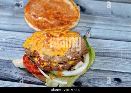 Ein saftiges, dickes, doppeltes Rinderpatty mit Käse, der mit Sauce bedeckt ist, knackigem Salat, frischen Tomaten, Zwiebeln und Gurken in einem großen Sesambrötchen, einem Rindfleisch Stockfoto