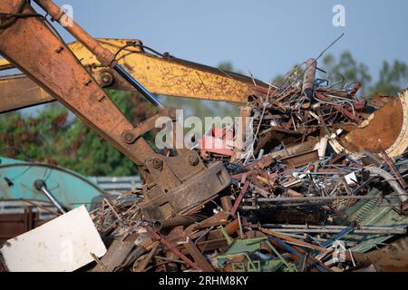 Magnet des Hydraulikbaggers hebt Stahlschrott aus dem Recyclingmaterialhaufen auf dem Schrottplatz in der Recyclingfabrik. Bagger mit Elektro- und Magnetsauger Stockfoto