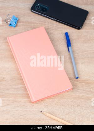 Nahaufnahme des Notebooks, ein blauer Stift, ein Telefon auf einem Holztisch sind bereit für den Unterricht. Schreibwaren. Zurück zur Schule Stockfoto