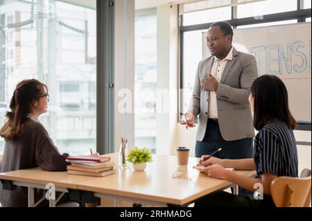 Ein professioneller und freundlicher afroamerikanischer Lehrer, der Englisch für asiatische Schüler in der Klasse an einer Sprachschule unterrichtet. Sprachzentrum, Engl Stockfoto