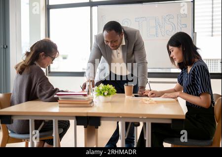 Ein professioneller Afro-amerikanischer Englischlehrer unterrichtet asiatische Schüler im Klassenzimmer an einer Sprachschule. Bildungskonzept Stockfoto