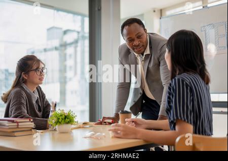 Ein professioneller afroamerikanischer Lehrer, der Englisch für asiatische Schüler in der Klasse an einer Sprachschule unterrichtet. Stockfoto
