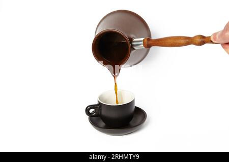 Mann, der Kaffee in eine Tasse gießt, isolierter weißer Hintergrund. Clay Cezve für die Kaffeezubereitung in der Hand Stockfoto
