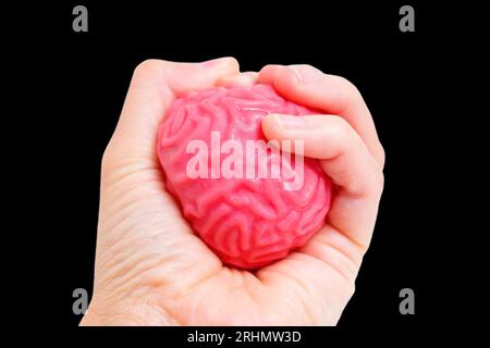 Hand, die ein biegsames geleeartiges menschliches Gehirnmodell fest zusammendrückt, isoliert auf Schwarz. Druck in der beruflichen Umgebung, starke mentale Belastung, Herausforderung für den Job Stockfoto