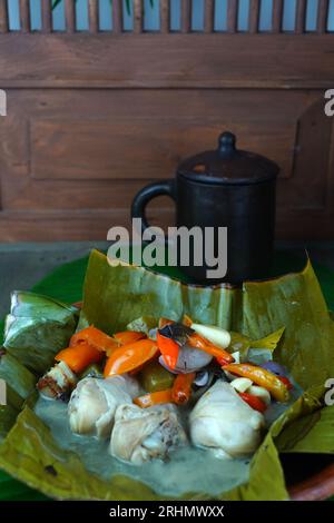 Garang ASEM, das traditionelle javanische Essen, wird auf einem Tonteller serviert, der mit Bananenblättern gesäumt ist und von einer Mischung aus Vogelaugen-Chili und Tomate begleitet wird Stockfoto