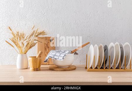 Holztrockner mit Tellern, große Schüssel mit Handtuch, verschiedene Küchenutensilien im Inneren einer modernen Küche in hellen Farben Stockfoto