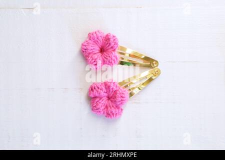 Pinkfarbene Blumen, die mit Häkeln gestrickt wurden, als Haarspangen, auf einem alten weißen Holztisch Stockfoto