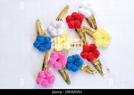 Mehrere bunte Blumen, die mit Häkelarbeit, als Haarspangen, auf einem alten weißen Holztisch gestrickt wurden Stockfoto