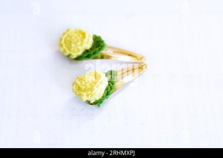 Gelbe Blumen, gestrickt mit Häkeln, als Haarspangen, auf einem alten weißen Holztisch. Selektiver Fokus. Stockfoto